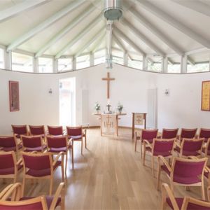 Ein heller, moderner Kirchenraum mit Holzstühlen und einem zentralen Altar mit Kreuz lädt zur stillen Besinnung ein.