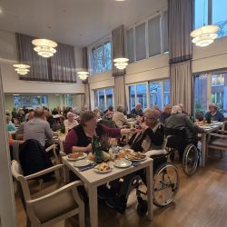 In einem hell erleuchteten Speisesaal genießen Menschen an einem gemütlichen Novemberabend gemeinsam ein festliches Essen.