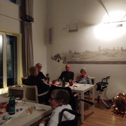 Eine Gruppe älterer Menschen genießt ein gemütliches Beisammensein an einem festlich gedeckten Tisch in einem warm beleuchteten Raum.