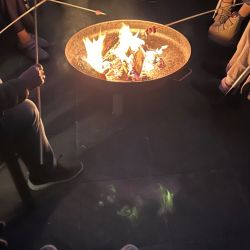 Menschen rösten Marshmallows über einem knisternden Lagerfeuer in einer Feuerschale und genießen die gemütliche Atmosphäre.