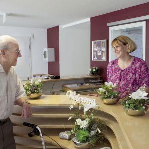 Ein älterer Mann unterhält sich lächelnd mit einer Frau an einer blumengeschmückten Rezeption im Posener-Stil.