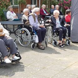 Ältere Menschen in Rollstühlen unterhalten sich fröhlich im sonnigen Garten eines Altenheims.