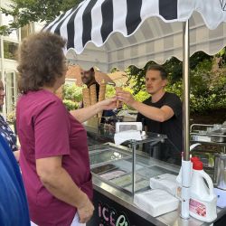 Eine Frau kauft ein Eis von einem Verkäufer an einem schwarz-weiß gestreiften Eiswagen im Freien.