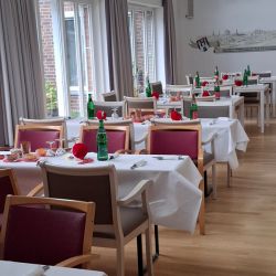 Ein festlich gedeckter Speisesaal mit weißen Tischdecken und roten Akzenten erwartet Gäste für ein besonderes Ereignis.