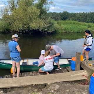 Eine Gruppe von Menschen bereitet sich darauf vor, an einem ruhigen Flussufer in einem Kanu abzulegen.