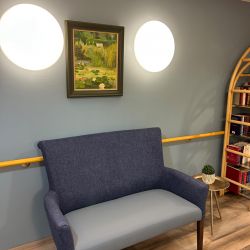 Ein blaues Sofa steht vor einer blauen Wand mit einem Gemälde und zwei runden Lampen darüber.