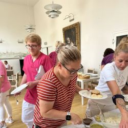 Menschen bedienen sich an einem Buffet mit Pizza und Lachs in einem hellen Raum, während sie ihre Teller füllen.