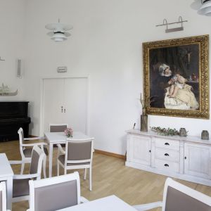 Ein eleganter Raum mit weißen Tischen und Stühlen, einem Klavier und einem großen Gemälde an der Wand.