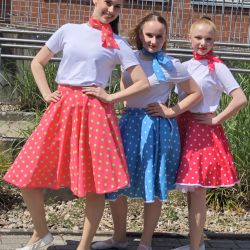 Drei junge Tänzerinnen strahlen in bunten, gepunkteten Röcken bei einem fröhlichen Aerobic-Auftritt im Altenheim.