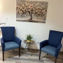 Zwei blaue Sessel flankieren einen kleinen Tisch mit Pflanze vor einem Gemälde eines blühenden Baumes an der Wand.