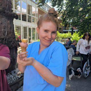 Eine lächelnde Frau in blauer Kleidung genießt ein Eis im Freien bei sonnigem Wetter.