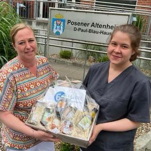 Zwei Frauen präsentieren mit Freude vor dem Posener Altenheim einen großen Präsentkorb voller Geschenke.