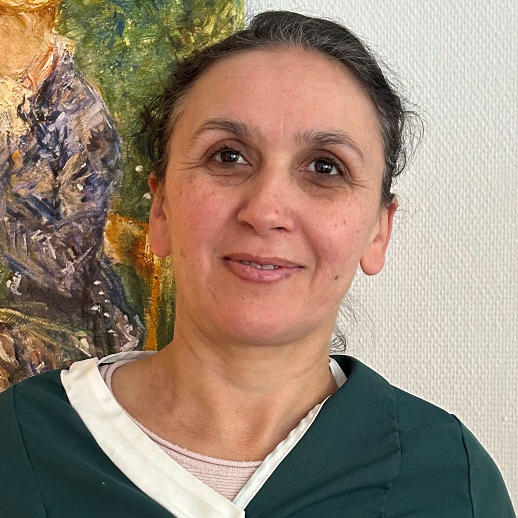 Eine Frau lächelt vor einem farbenfrohen Gemälde, das die Wand in leuchtenden Farben schmückt.