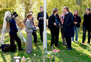 Eine Gruppe von Menschen diskutiert angeregt auf einer Wiese, während eine Kamera die lebhafte Szene aufnimmt.