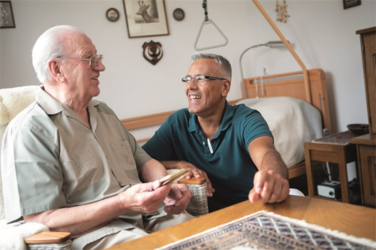 Ein älterer Mann und ein jüngerer Mann lachen herzlich in einem gemütlichen Raum, während sie ein Fotoalbum betrachten.